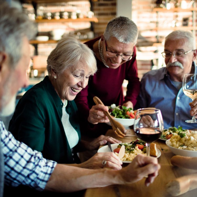 A group of older friends laughing together over a shared meal at the dinner table