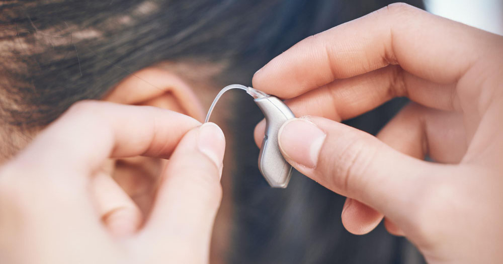 A receiver-in-canal hearing aid being placed behind the ear